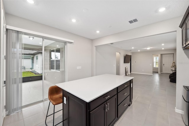 kitchen featuring a kitchen bar, dark brown cabinets, a center island, and light tile patterned flooring