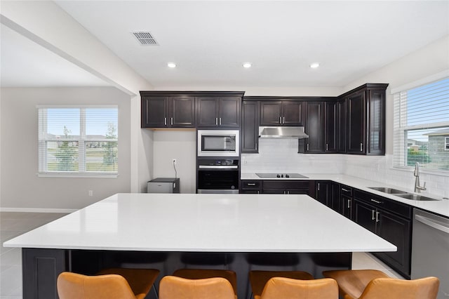 kitchen with a kitchen bar, stainless steel appliances, a kitchen island, and sink