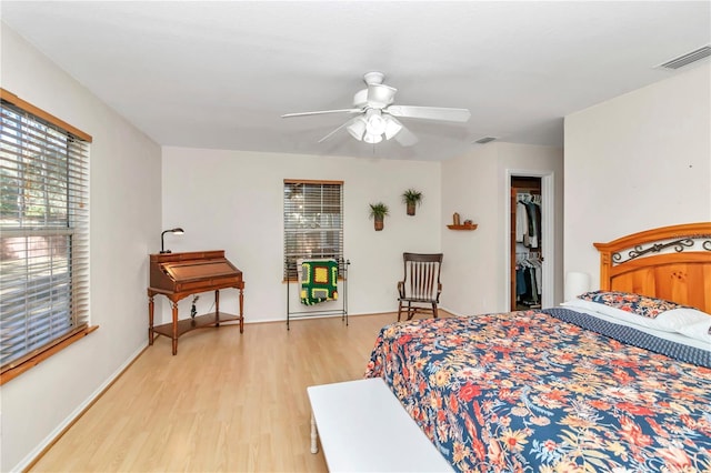 bedroom featuring a walk in closet, light hardwood / wood-style flooring, a closet, and ceiling fan