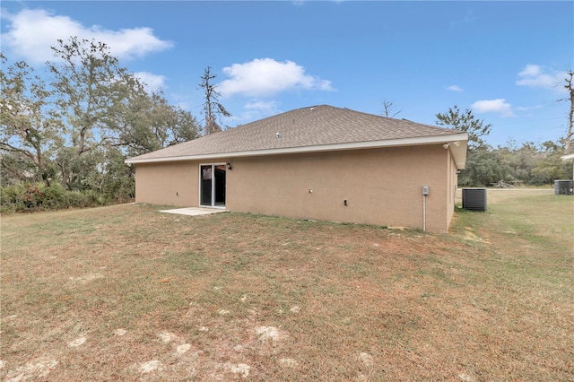 rear view of property with central AC unit and a lawn