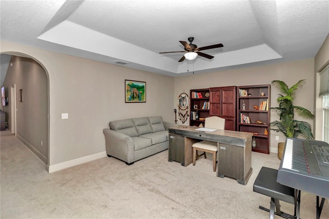 carpeted home office with ceiling fan, a textured ceiling, and a tray ceiling