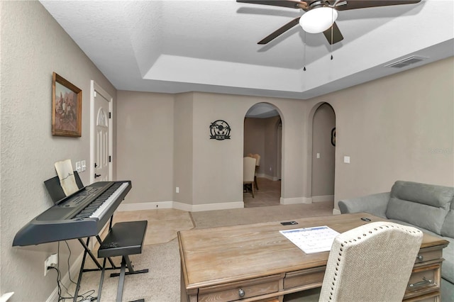 tiled office space featuring a raised ceiling, ceiling fan, and a textured ceiling