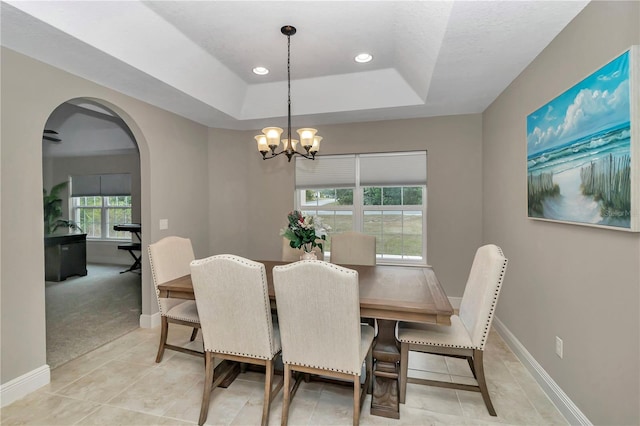 dining space with a tray ceiling, light carpet, and a notable chandelier