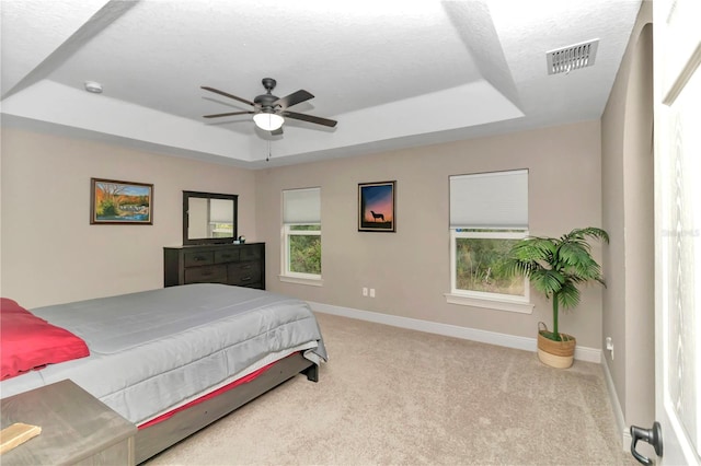 bedroom featuring a textured ceiling, light colored carpet, a raised ceiling, and ceiling fan