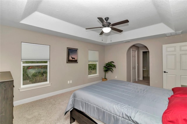 carpeted bedroom with a raised ceiling, ceiling fan, and a textured ceiling