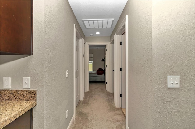 corridor featuring a textured ceiling and light colored carpet