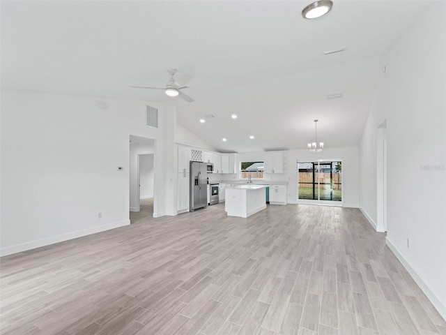 unfurnished living room with ceiling fan with notable chandelier, light hardwood / wood-style floors, high vaulted ceiling, and sink