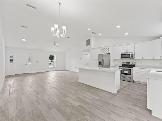 kitchen featuring pendant lighting, white cabinets, stainless steel appliances, and ceiling fan with notable chandelier