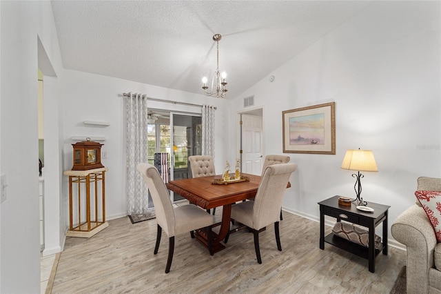 dining room featuring a textured ceiling, vaulted ceiling, an inviting chandelier, and light hardwood / wood-style flooring