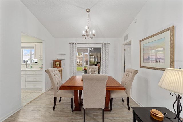 dining area featuring sink, a chandelier, vaulted ceiling, and light wood-type flooring