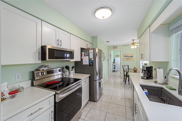 kitchen featuring sink, light tile patterned flooring, a textured ceiling, white cabinets, and appliances with stainless steel finishes