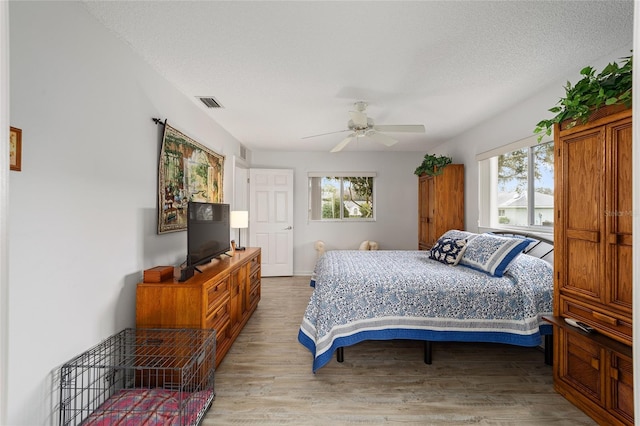 bedroom with multiple windows, ceiling fan, a textured ceiling, and hardwood / wood-style flooring