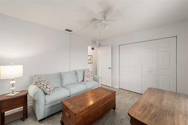 living room featuring ceiling fan, light hardwood / wood-style flooring, and a textured ceiling