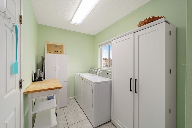 clothes washing area with light tile patterned flooring, cabinets, separate washer and dryer, and a textured ceiling