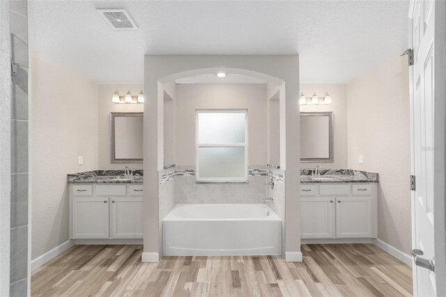 bathroom with hardwood / wood-style flooring, vanity, a tub to relax in, and a textured ceiling