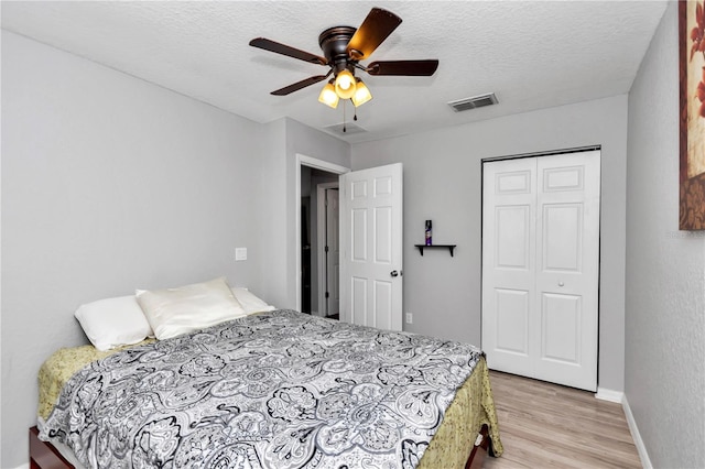 bedroom featuring a textured ceiling, light hardwood / wood-style flooring, a closet, and ceiling fan