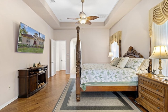 bedroom with ceiling fan, wood-type flooring, and a tray ceiling