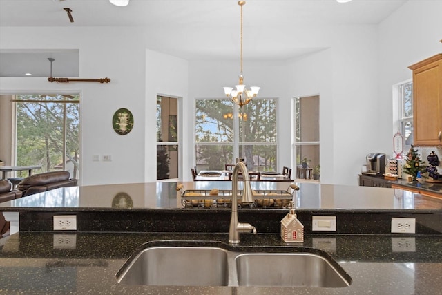 kitchen featuring pendant lighting, sink, an inviting chandelier, and dark stone countertops