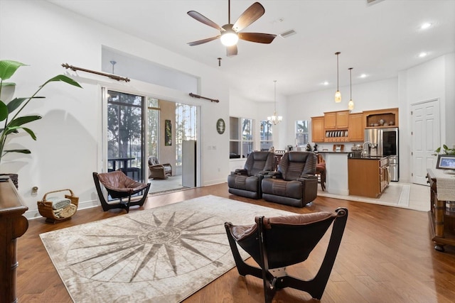 living room with a towering ceiling, ceiling fan with notable chandelier, and light wood-type flooring