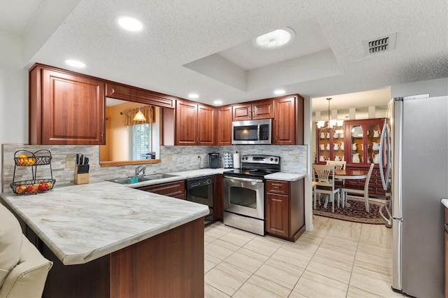 kitchen featuring kitchen peninsula, stainless steel appliances, a raised ceiling, sink, and a notable chandelier