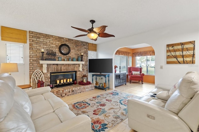 living room featuring ceiling fan, a textured ceiling, and a brick fireplace