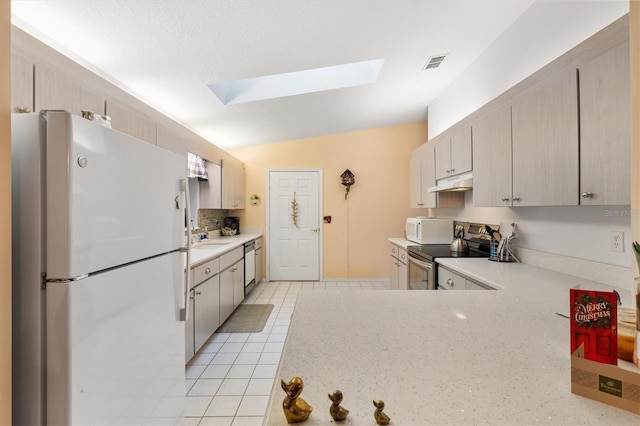 kitchen featuring sink, white appliances, lofted ceiling with skylight, and light tile patterned flooring