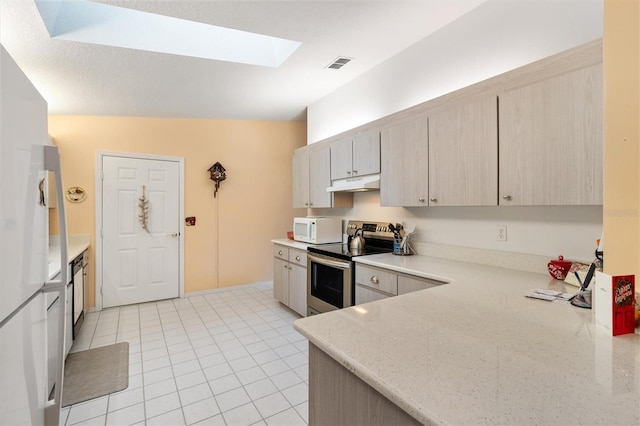 kitchen featuring a skylight, stainless steel appliances, light stone counters, light brown cabinetry, and light tile patterned floors