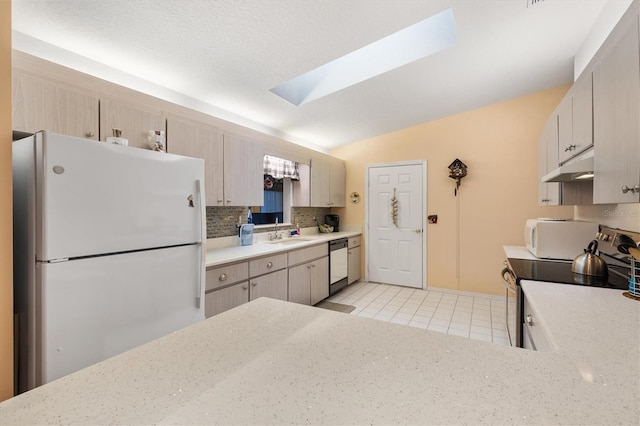 kitchen with sink, white appliances, decorative backsplash, vaulted ceiling with skylight, and light tile patterned floors