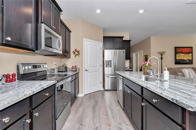 kitchen featuring sink, appliances with stainless steel finishes, dark brown cabinetry, light stone counters, and light wood-type flooring