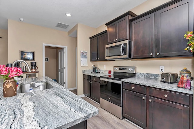 kitchen with dark brown cabinetry, sink, light stone counters, light wood-type flooring, and stainless steel appliances