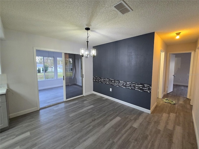 unfurnished dining area with a notable chandelier, dark hardwood / wood-style flooring, and a textured ceiling