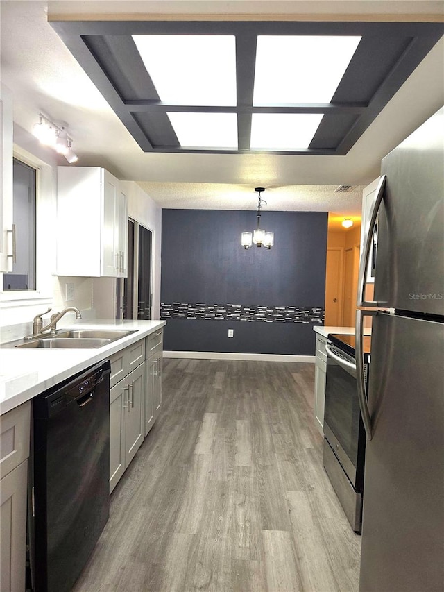 kitchen with appliances with stainless steel finishes, light wood-type flooring, sink, white cabinetry, and hanging light fixtures