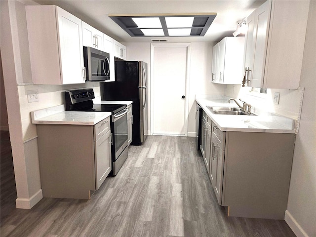 kitchen with sink, white cabinetry, stainless steel appliances, and light hardwood / wood-style flooring