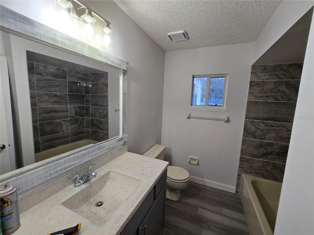 full bathroom featuring wood-type flooring, a textured ceiling, toilet, vanity, and tiled shower / bath