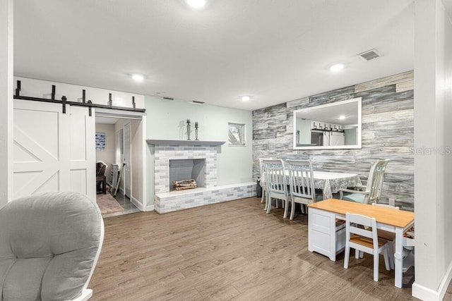 dining area with a barn door, light wood-type flooring, and a brick fireplace