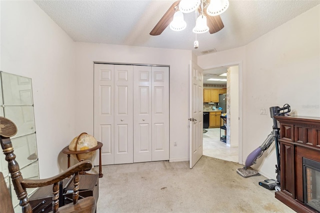 living area with ceiling fan, light colored carpet, and a textured ceiling