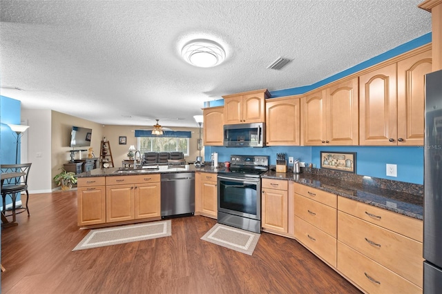 kitchen featuring dark wood-type flooring, dark stone counters, sink, appliances with stainless steel finishes, and kitchen peninsula