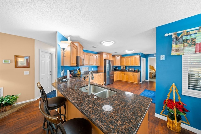 kitchen featuring kitchen peninsula, appliances with stainless steel finishes, sink, dark hardwood / wood-style floors, and a breakfast bar area