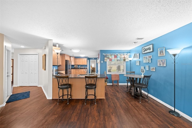 kitchen with a textured ceiling, dark hardwood / wood-style flooring, a kitchen bar, kitchen peninsula, and stainless steel refrigerator