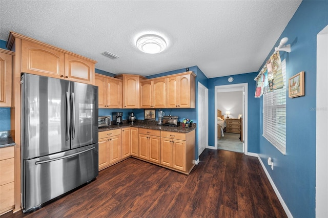 kitchen with light brown cabinets, dark wood-type flooring, dark stone countertops, a textured ceiling, and stainless steel refrigerator