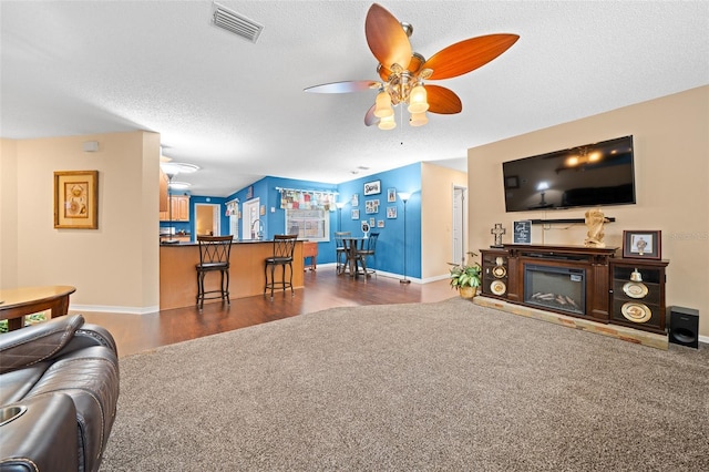 living room featuring a textured ceiling, ceiling fan, indoor wet bar, and dark colored carpet