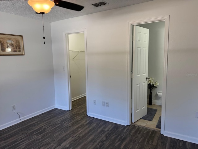 unfurnished bedroom with a textured ceiling, ceiling fan, dark wood-type flooring, a spacious closet, and a closet