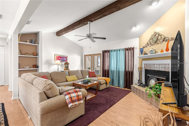 living room with hardwood / wood-style floors, vaulted ceiling with beams, ceiling fan, and a tiled fireplace