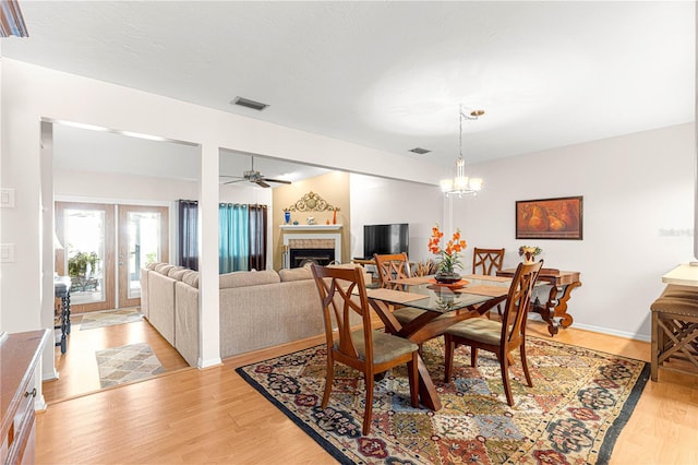 dining room featuring ceiling fan with notable chandelier, light hardwood / wood-style floors, a tile fireplace, and french doors