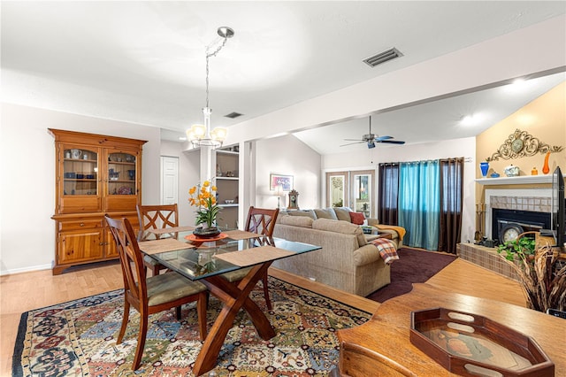 dining room featuring hardwood / wood-style floors, vaulted ceiling with beams, ceiling fan with notable chandelier, and a tiled fireplace