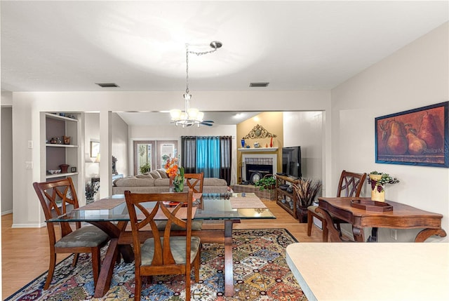 dining area featuring french doors, light wood-type flooring, a fireplace, and an inviting chandelier