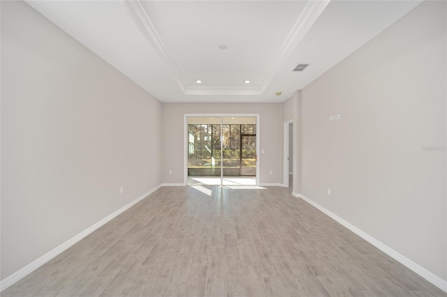 empty room featuring light hardwood / wood-style floors, a raised ceiling, and ornamental molding