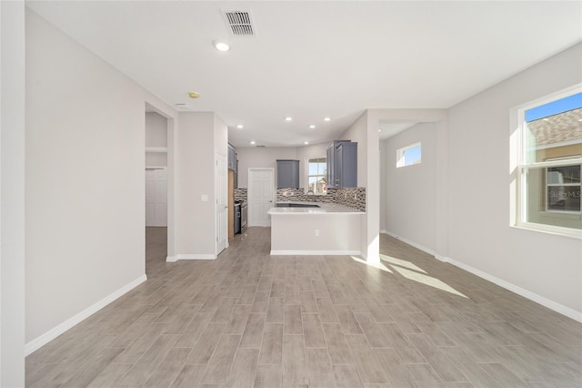 kitchen featuring kitchen peninsula, decorative backsplash, light hardwood / wood-style flooring, and gray cabinetry