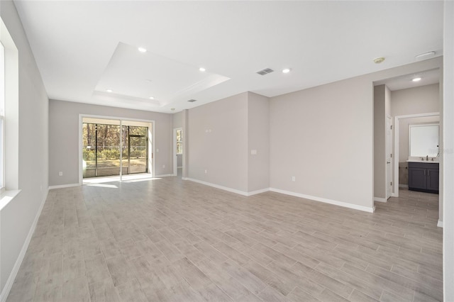 empty room featuring light wood-type flooring, sink, and a tray ceiling