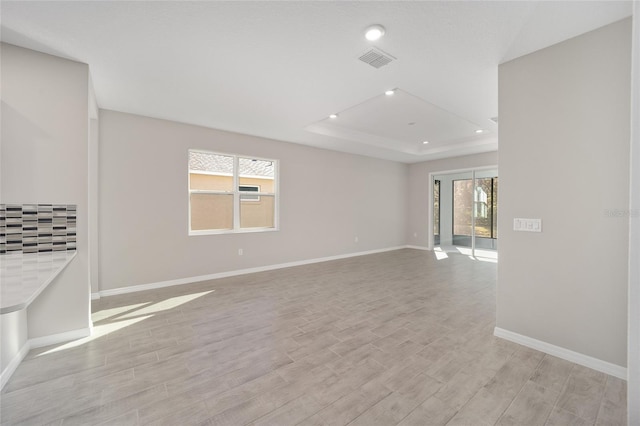 spare room featuring a tray ceiling, a wealth of natural light, and light hardwood / wood-style floors